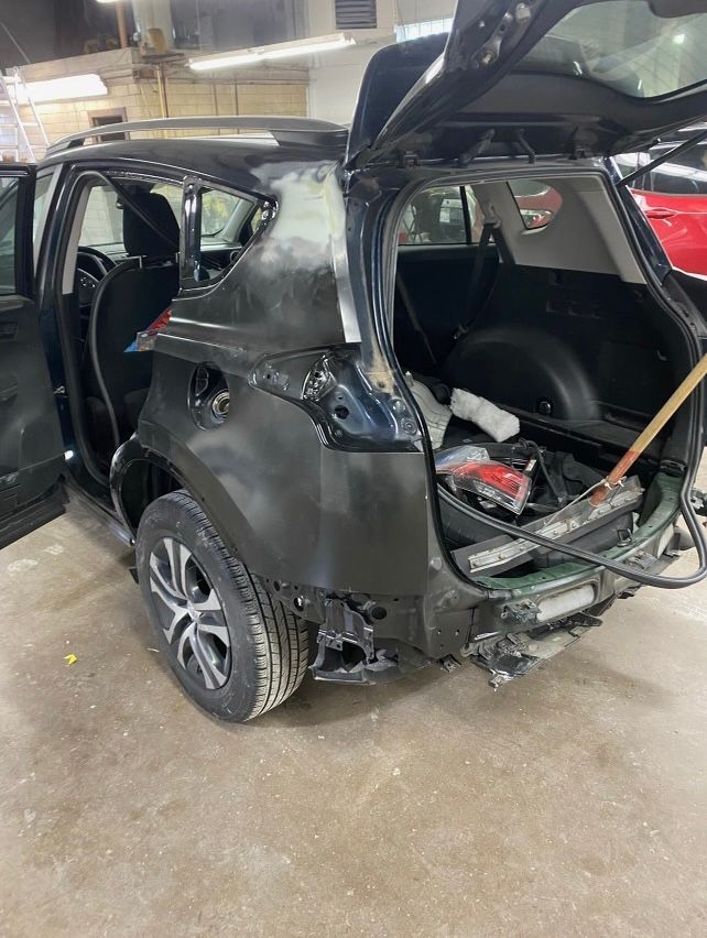 Black SUV with rear damage and open hatch in a repair shop.