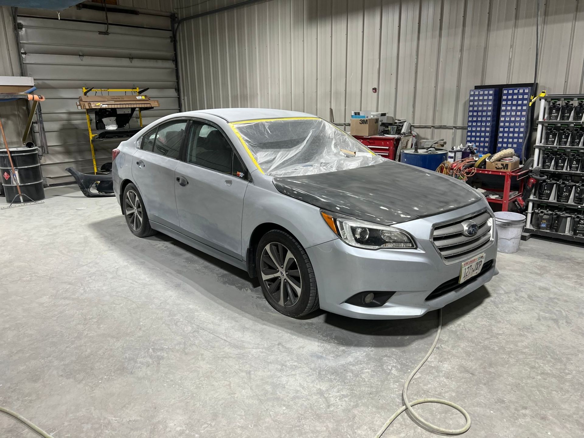 Silver sedan in a body shop, hood masked, ready for paint.
