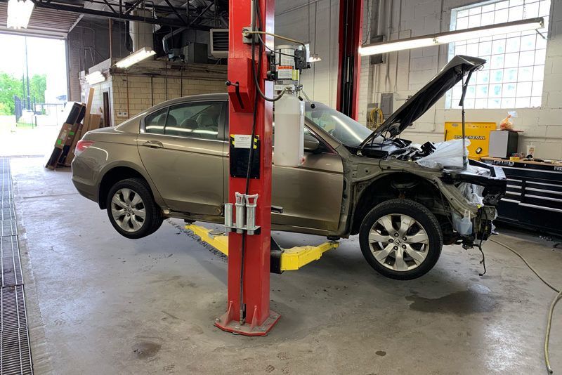 A car on a lift in a garage, with the hood open and parts missing.