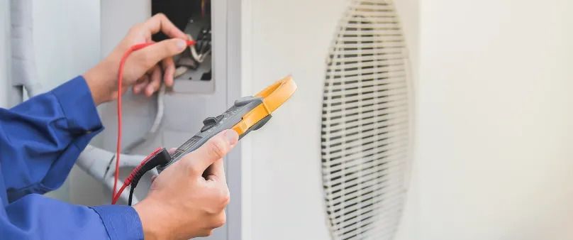 Technician testing an electrical outlet with a multimeter next to a wall vent
