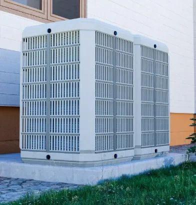 Large white outdoor HVAC unit beside a building wall, on a concrete pad near grass.