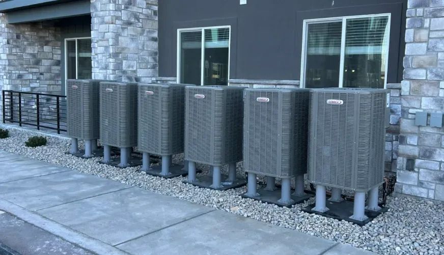Row of gray outdoor utility units beside a stone building with windows.