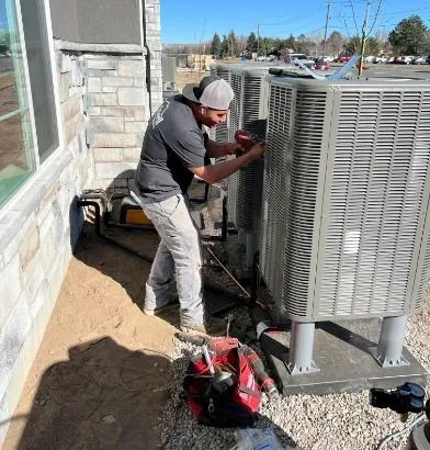 Technician working on outdoor HVAC unit beside a building, with tools on the ground.