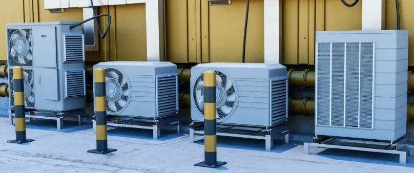 Row of outdoor HVAC units beside a yellow industrial building, separated by black-and-yellow bollards