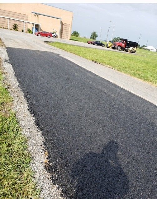 Newly paved asphalt driveway leading uphill with a building in the background