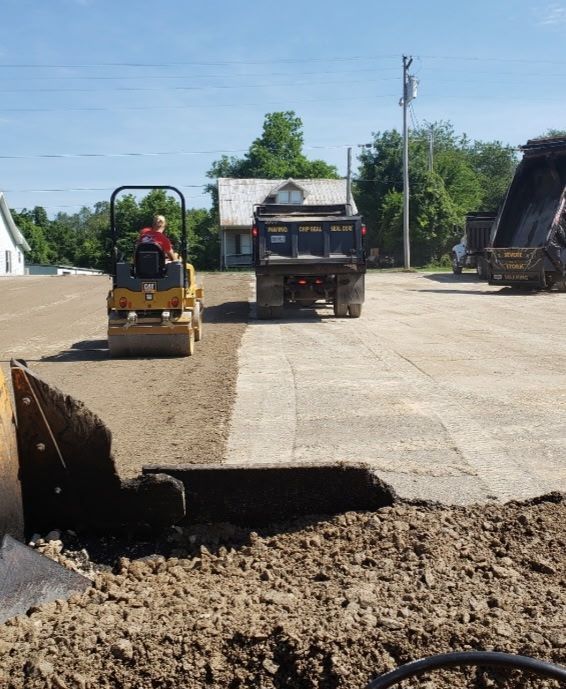 Road construction site: roller compacts asphalt, dump truck nearby