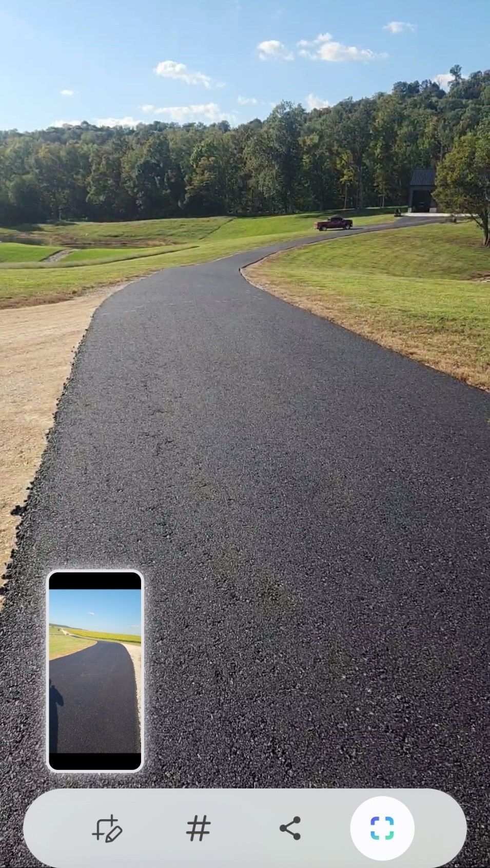 Asphalt path curving through a green field with trees in the background under a blue sky