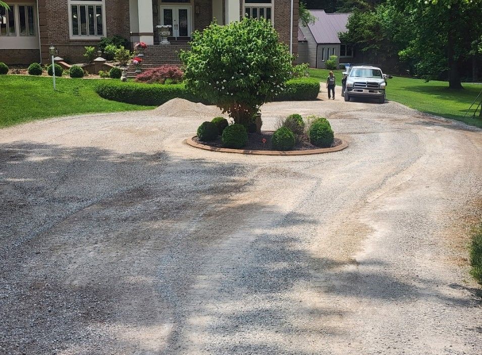 Gravel driveway leading to a house with a circular flowerbed and a truck; two people walk near the truck