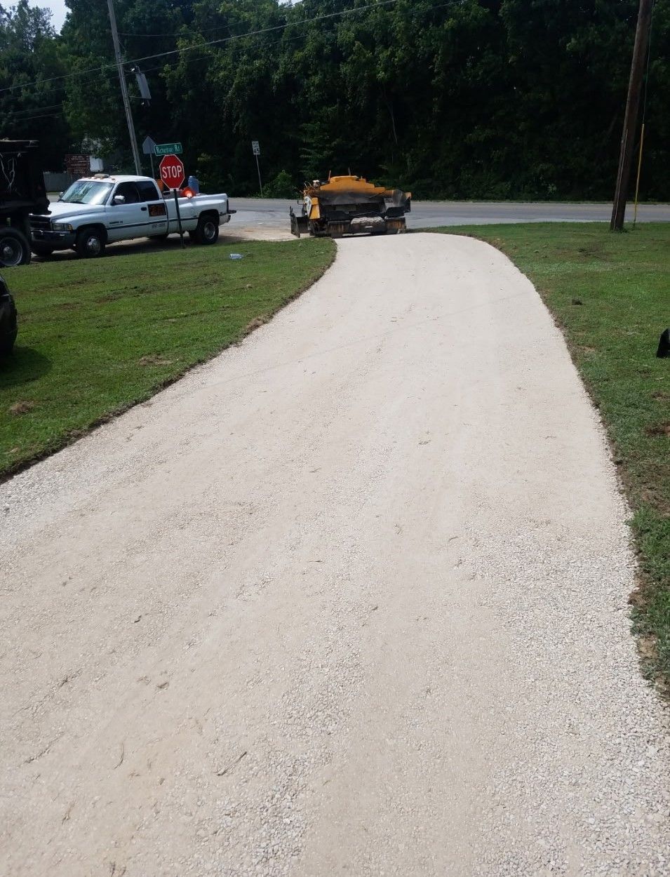 Newly paved gravel driveway, light tan color, with truck and equipment, adjacent to a green grassy area