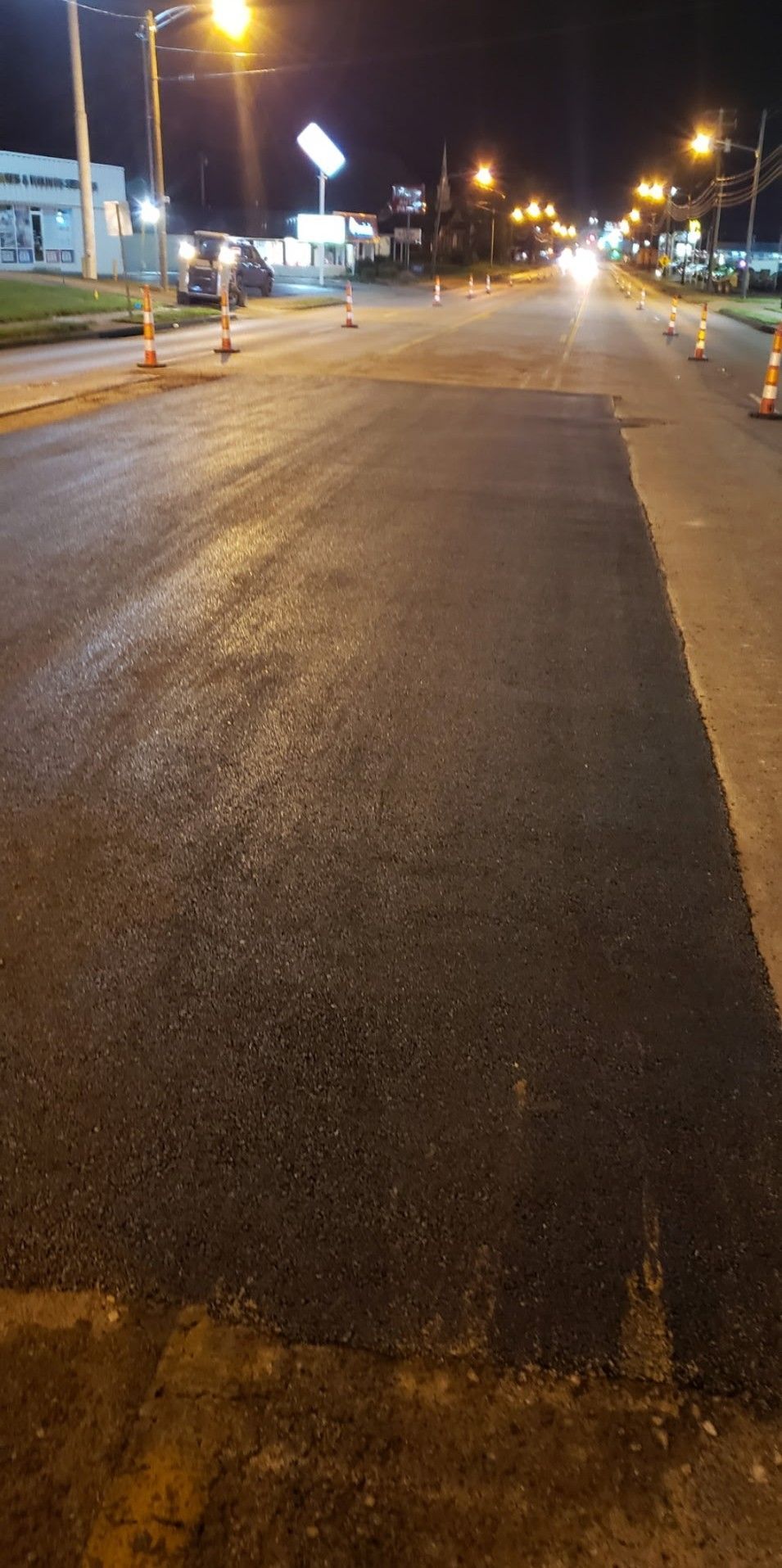 Newly paved road at night, with streetlights and traffic cones