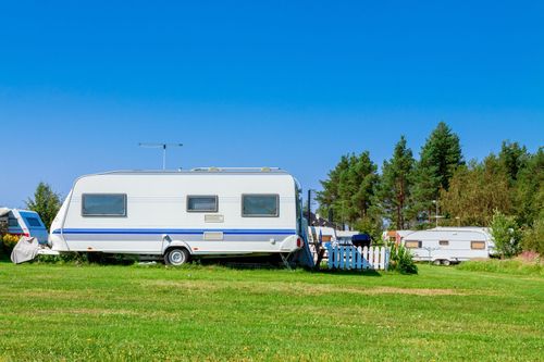 White travel trailer parked on a grassy field beside trees under a clear blue sky