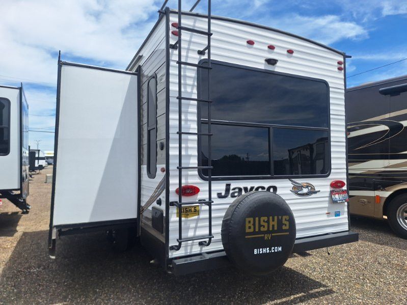 Rear view of a white Jayco travel trailer with slide-out extended and spare tire cover.