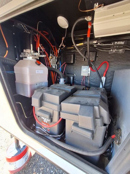 Battery bank and inverter wiring inside a vehicle compartment, with cables and coolant reservoir visible