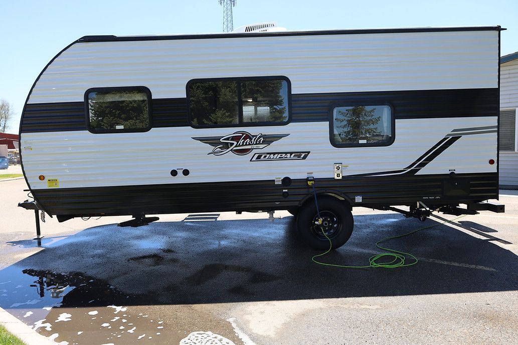 White travel trailer parked on a wet lot, with dark stripe accents and reflective windows.