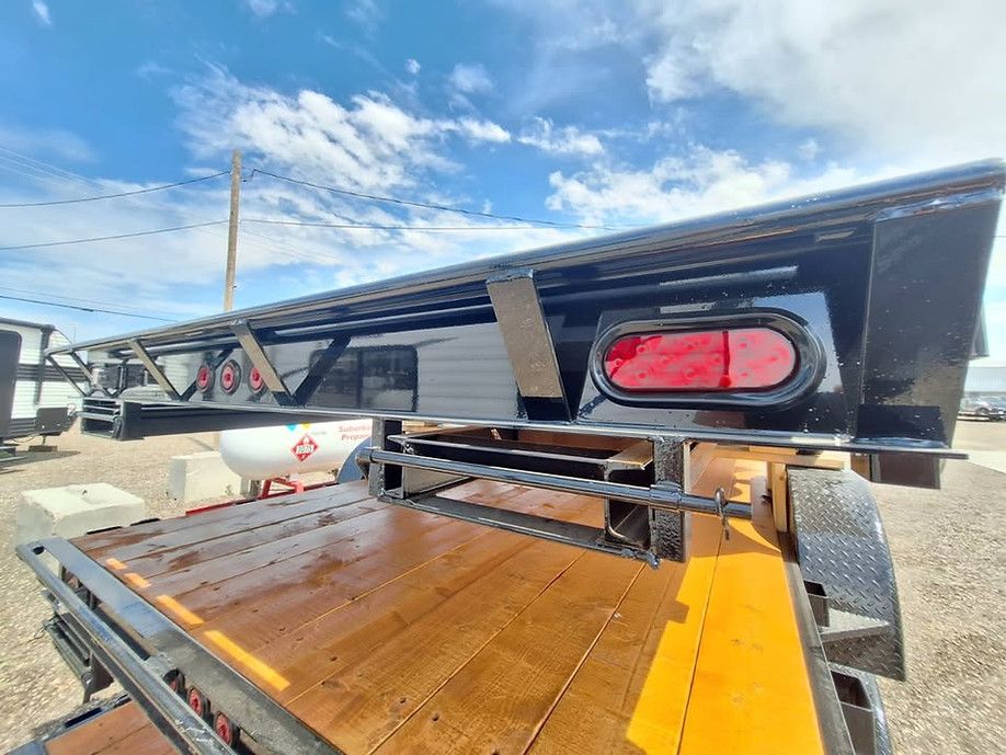 Black truck bed camper shell with a red rear window, parked on a trailer in an outdoor lot