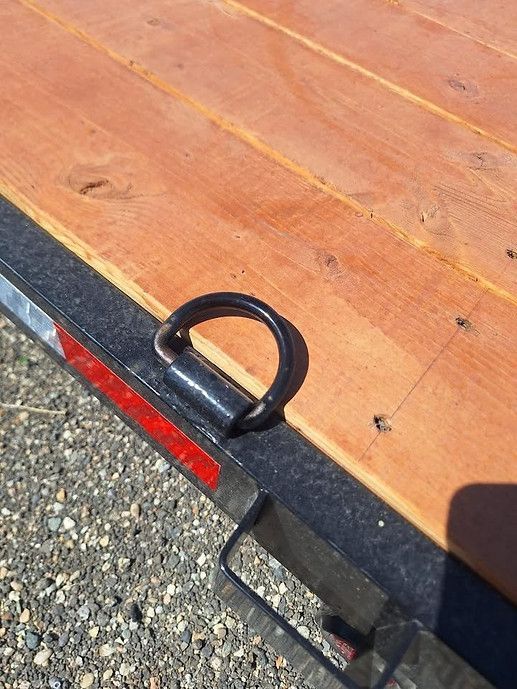 Black metal tie-down ring on a wooden trailer deck with gravel beside it