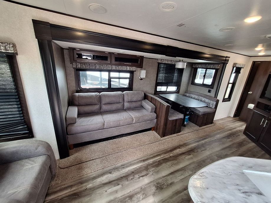 Compact living area with gray sofa, wood-look floor, and kitchen island in a modern RV interior