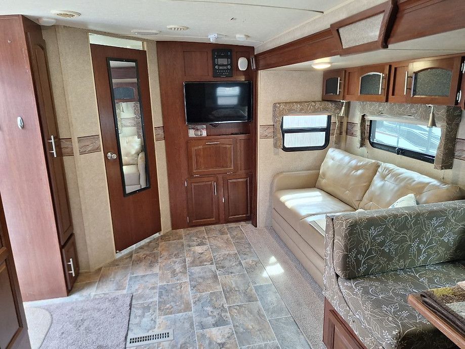 RV interior with tan sofa, wood cabinets, wall TV, and patterned floor.