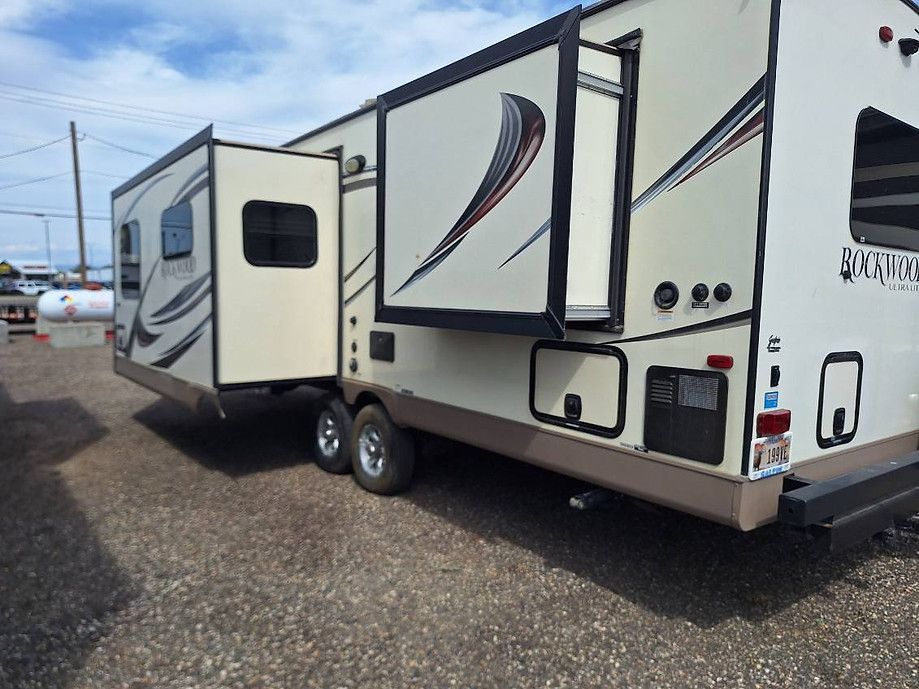 White travel trailer parked on gravel lot, with slide-out extended and abstract gray-and-black graphics.
