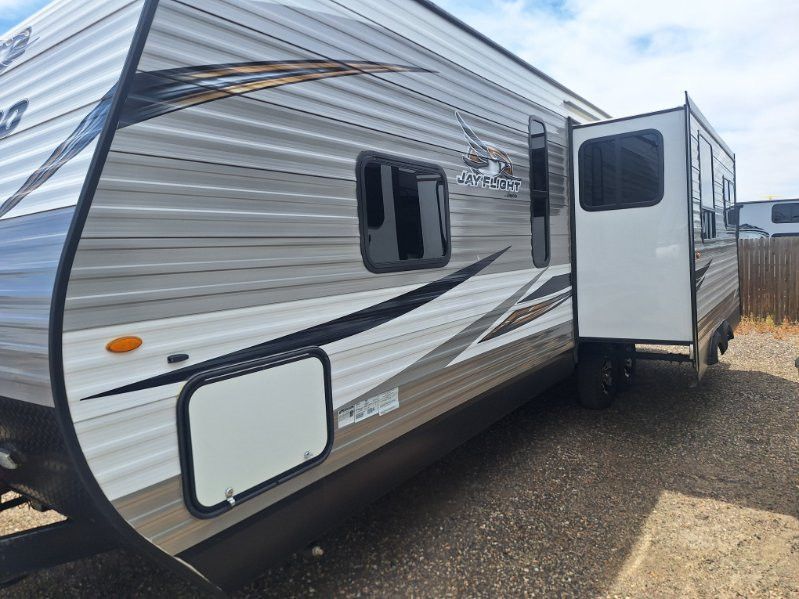 White travel trailer with black and gray stripes parked outdoors, side door open on a gravel lot