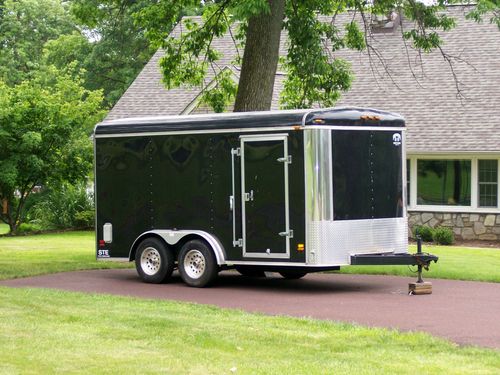 Black enclosed cargo trailer parked on a driveway beside a house and lawn