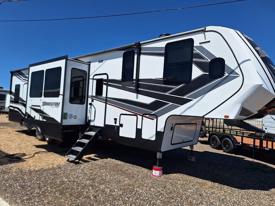 Large white and black fifth-wheel RV trailer parked on gravel under a clear blue sky.