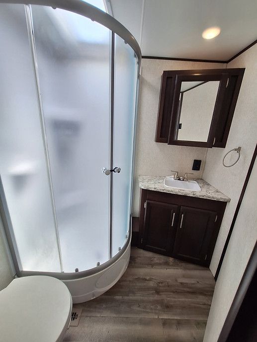 Small bathroom with curved frosted glass shower, dark vanity, mirror, and wood-look floor.