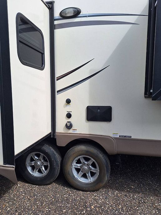 White RV trailer side with door, window, and twin wheels parked on gravel.