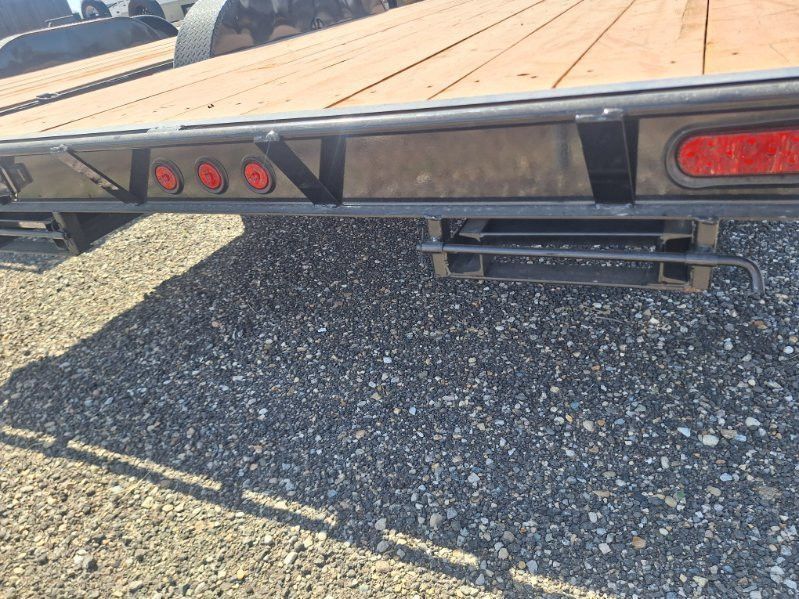 Rear view of a flatbed trailer with red lights and black undercarriage over gravel.