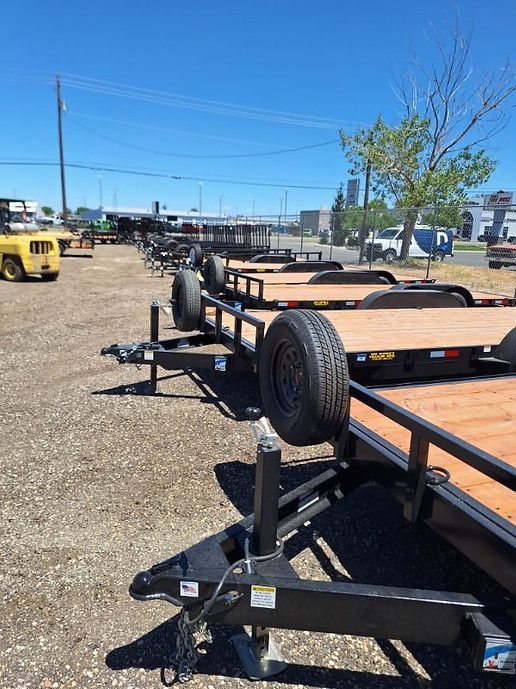Trailers parked in a gravel lot under a clear blue sky, with a yellow vehicle in the background.