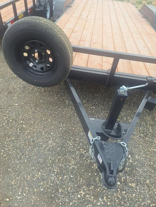 Black trailer wheel and hitch on a wooden deck over wet pavement.