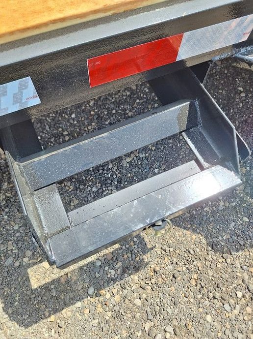 Metal step stool beside a vehicle, with a red reflector and gravel ground.