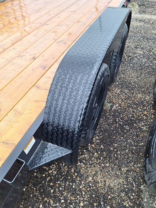 Black trailer wheel under a wooden deck, parked on gravel.