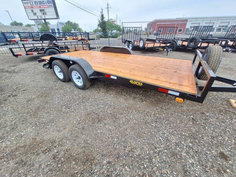Black flatbed utility trailer with wooden deck parked on a gravel lot at a trailer dealership