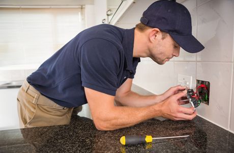 Technician installing an electrical outlet in a kitchen countertop wall opening