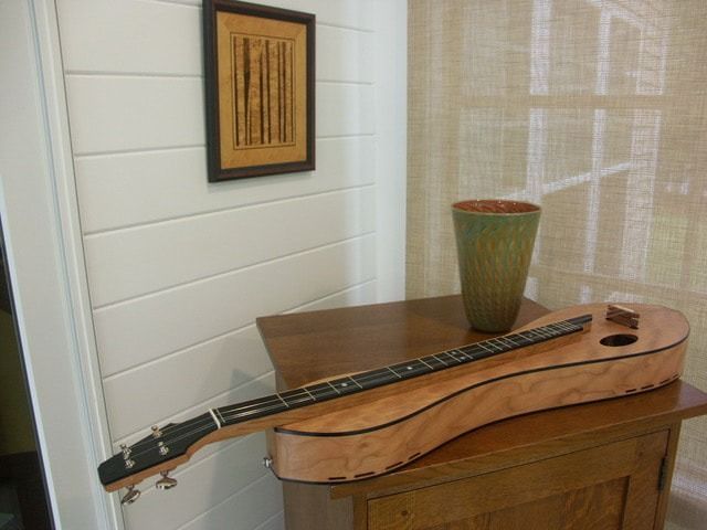 A guitar is sitting on top of a wooden cabinet next to a vase.