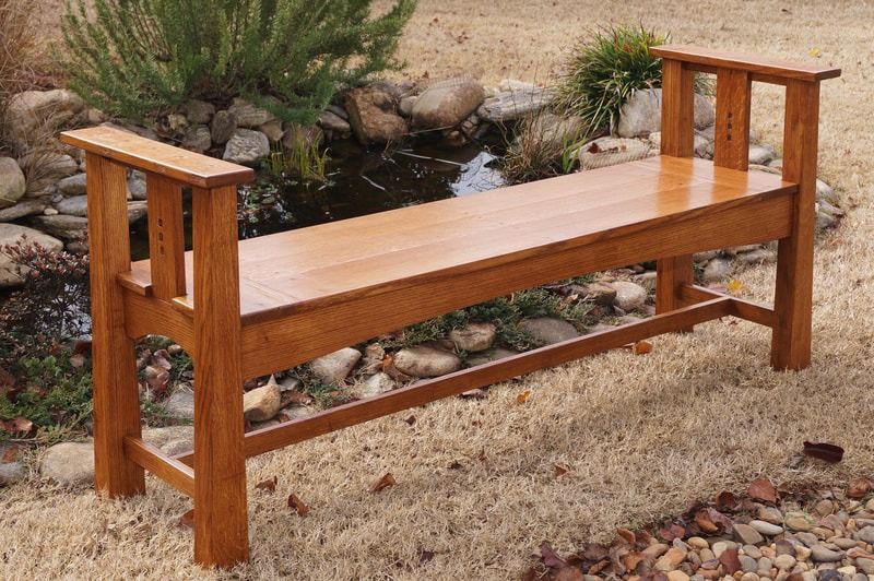 A wooden bench with arm rests is sitting in front of a pond.