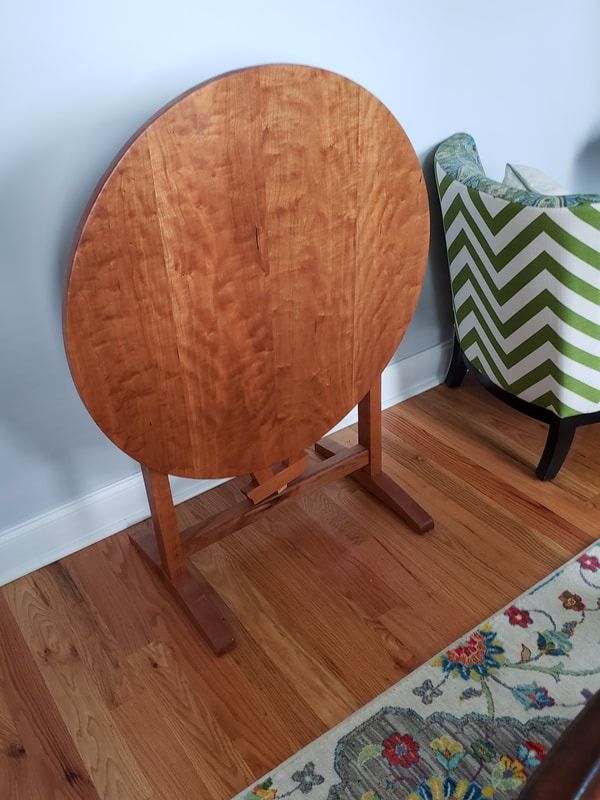 A round wooden table is sitting on a wooden floor next to a chair.