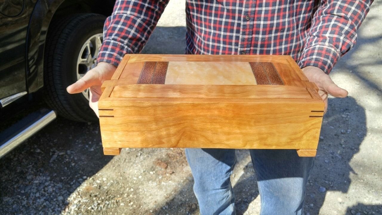 A man in a plaid shirt is holding a wooden box in his hands.