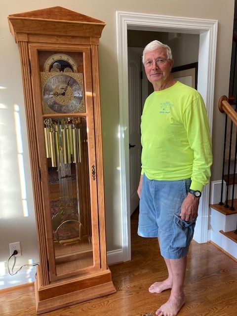 A man is standing in front of a grandfather clock in a living room.