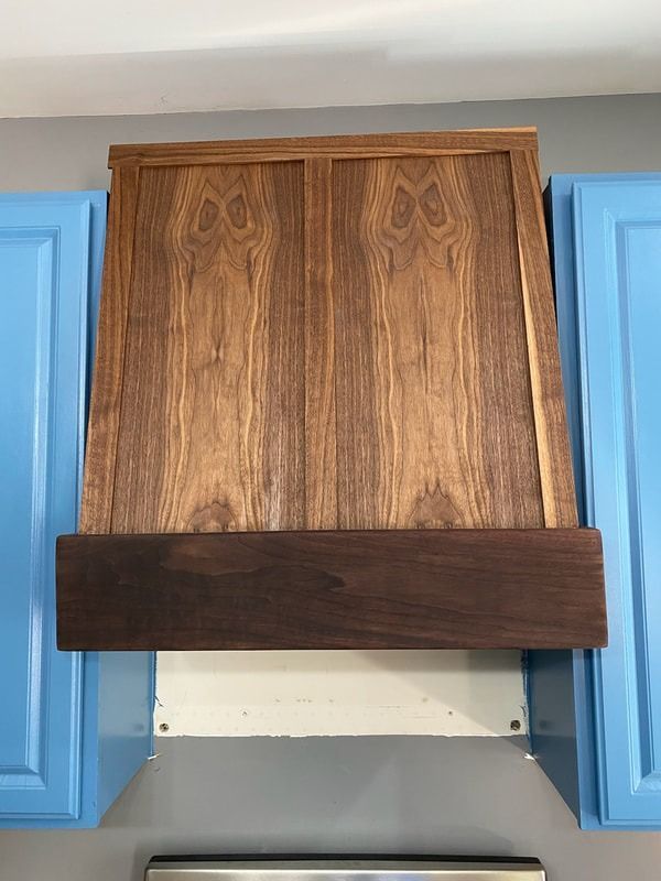 A kitchen with blue cabinets and a wooden hood above the stove.
