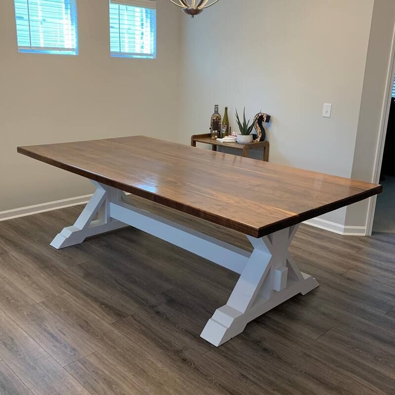 A wooden table with a white base is sitting in a dining room.