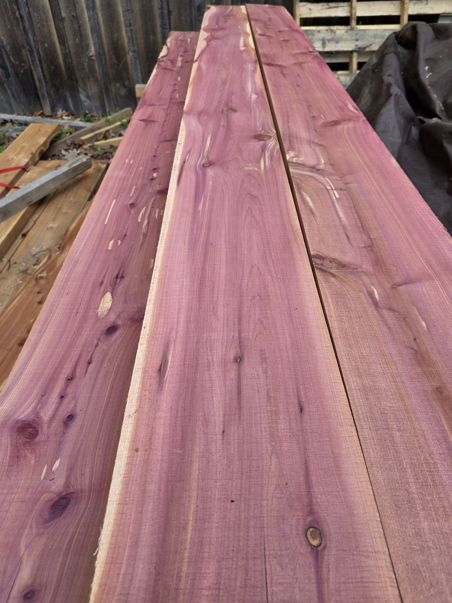 Stack of rough-cut eastern red cedar lumber showing distinct reddish-purple heartwood and dark knots.