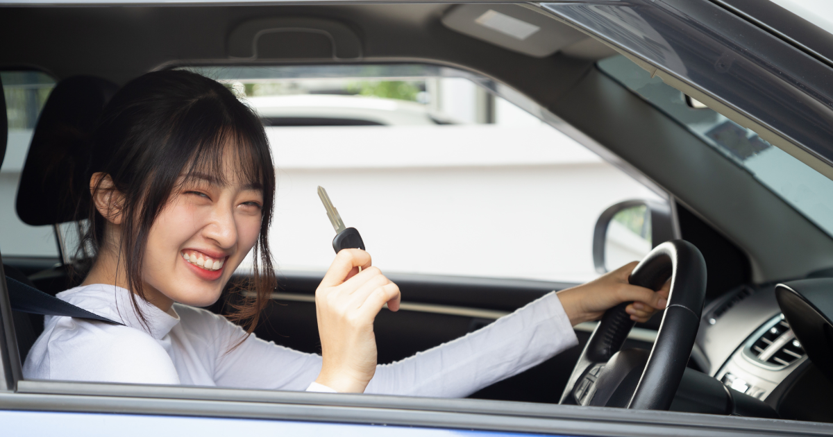 happy woman holding up her car key in the driver's seat