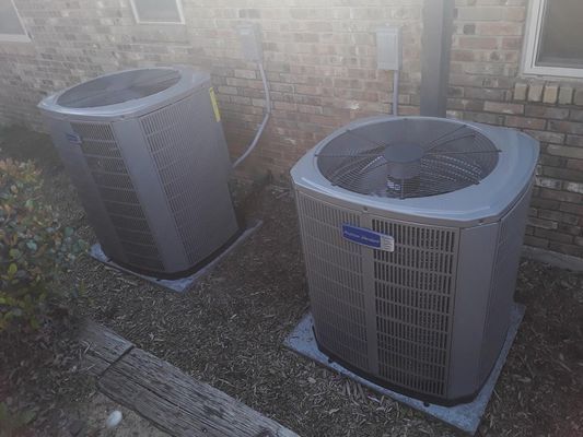 Two air conditioning units on concrete pads beside a brick building.