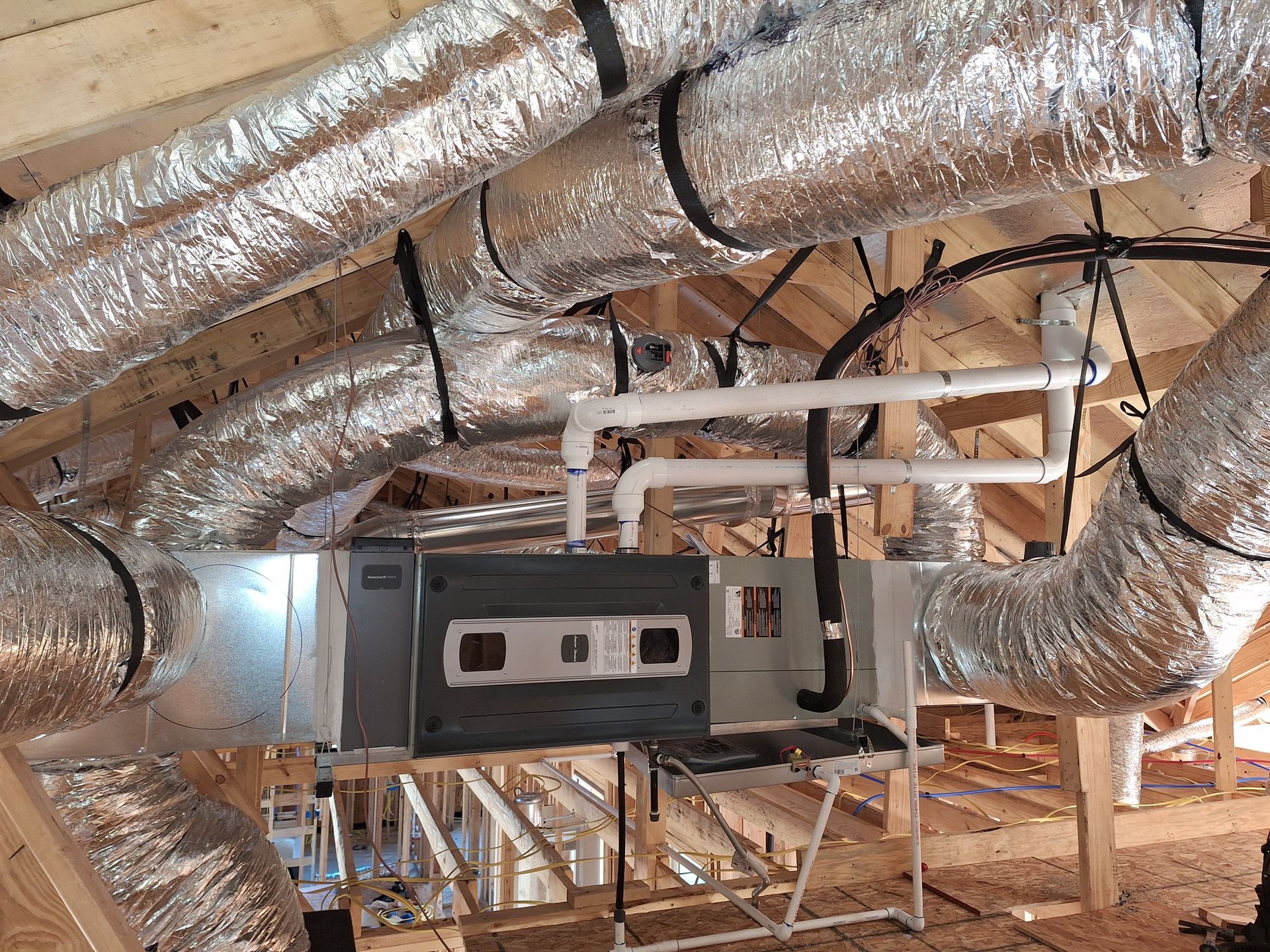 HVAC system in attic with silver ductwork, vents, and piping.