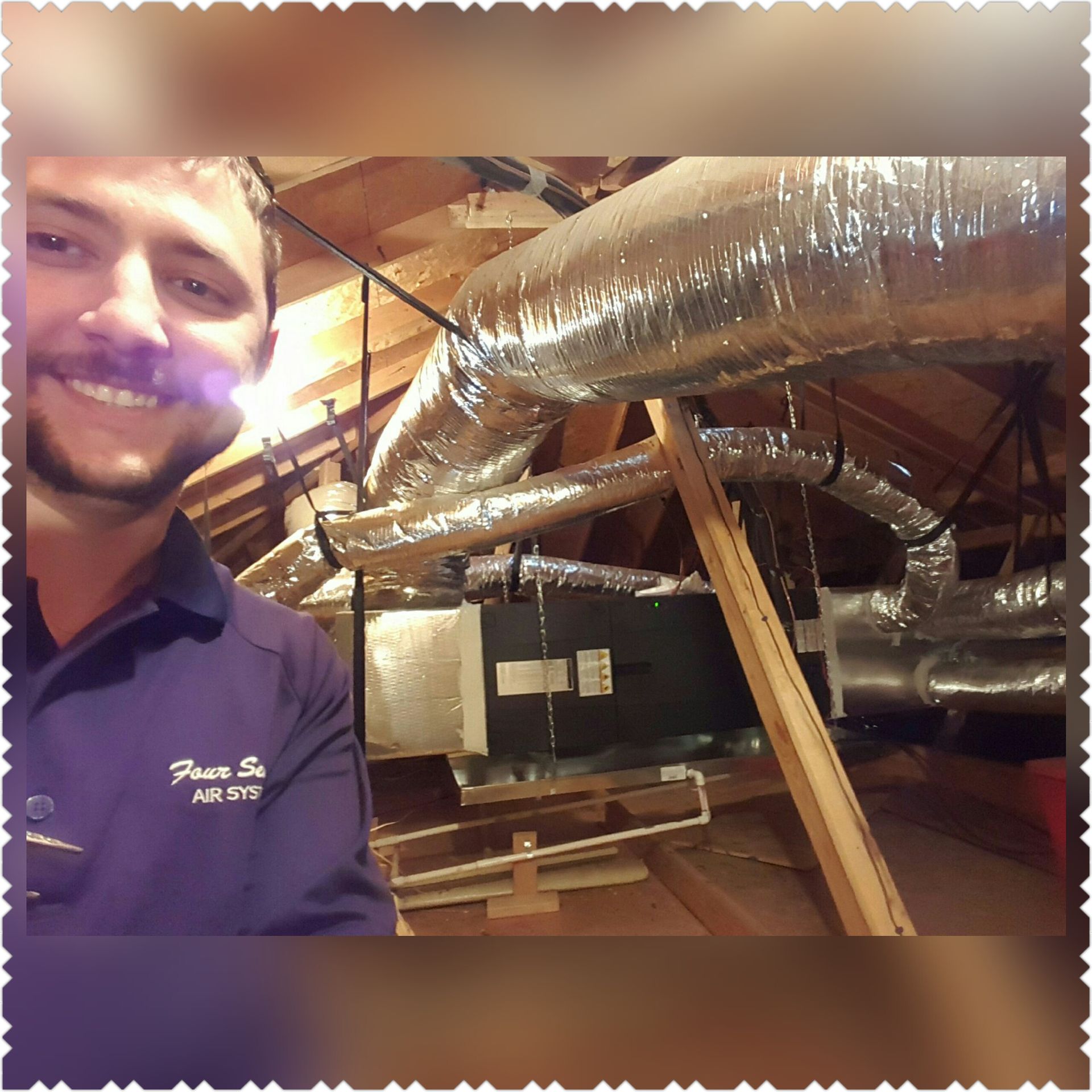 Man in purple shirt smiling in attic with HVAC system.