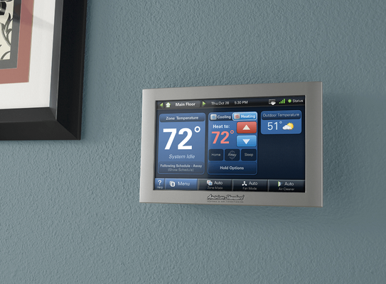 Silver smart thermostat on a light blue wall, displaying temperature and settings.