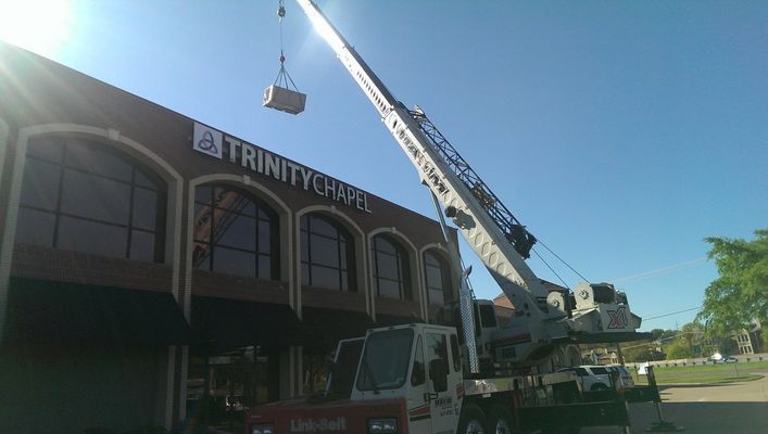 Crane lifting a box toward Trinity Church building on a sunny day.