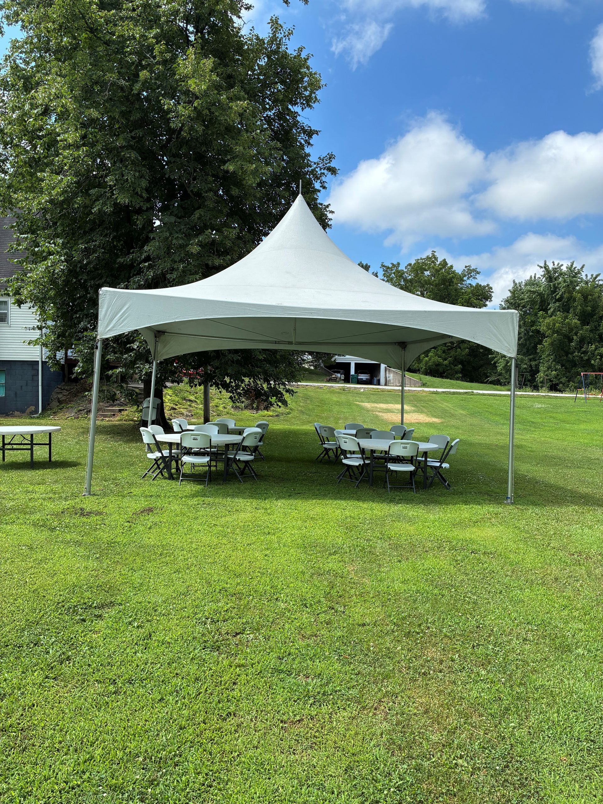 White canopy tent with picnic tables on a grassy lawn under a blue sky.